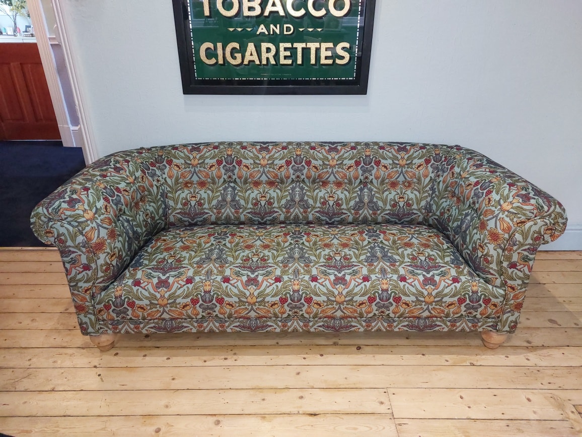 A curved channel-back banquette in soft grey fabric around a round timber dining table, recently completed in the workshop