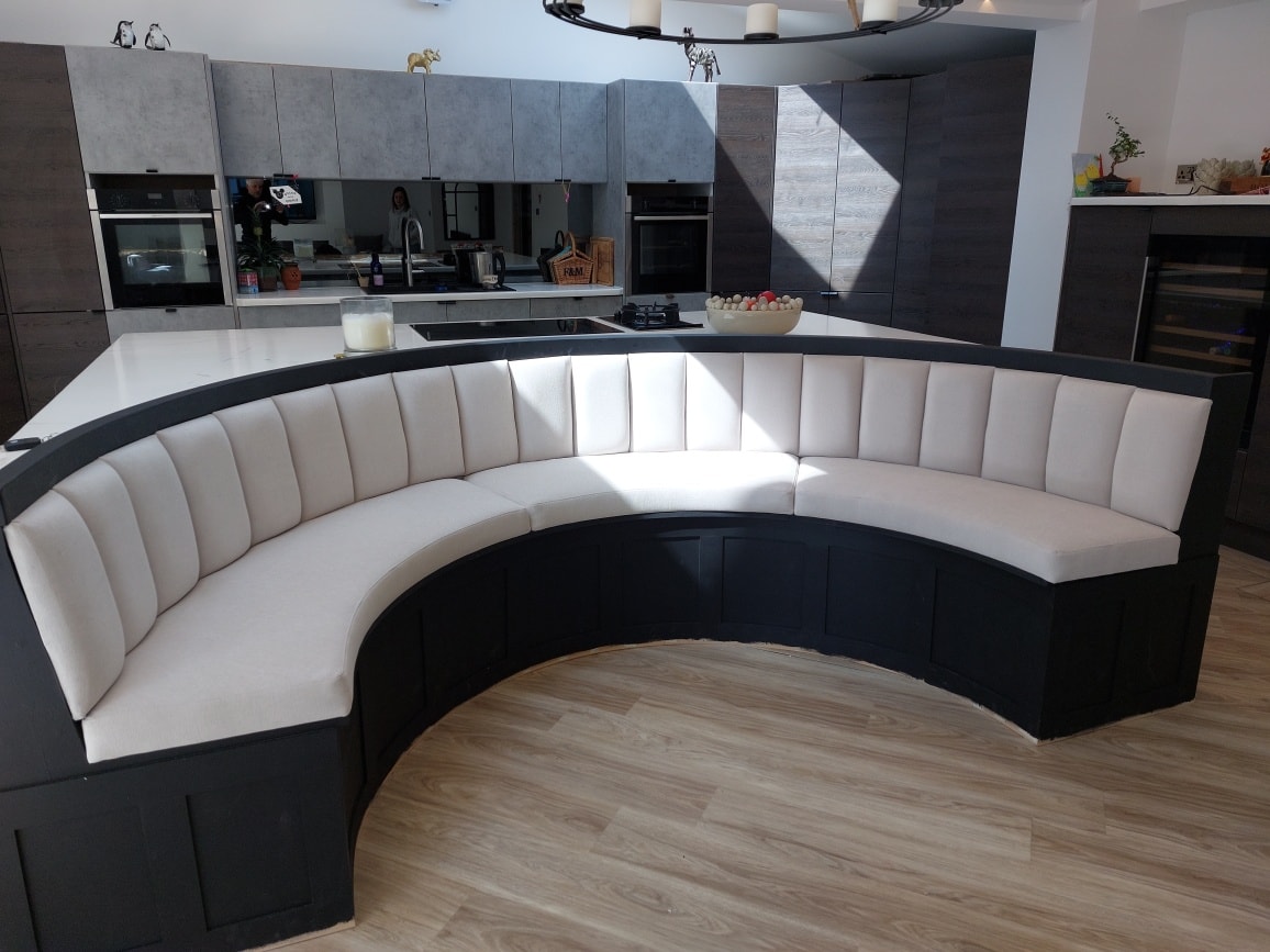 A curved channel-back banquette in white upholstery and black timber, built into a kitchen island